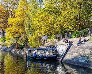 Colorful Trees Prints: Young people relax in the Autumn sun next to the Landwehr canal & people enjoy pleasure boat