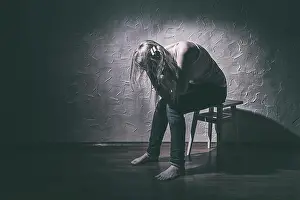 Sensitive Prints: Young sad woman sitting alone in a chair in an empty room