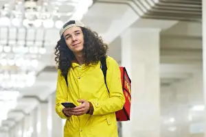 Texting Prints: Young smiling deliveryman in yellow jacket standing at subway station