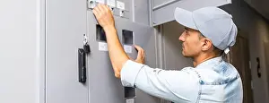 Repairman Prints: Young smiling electrician doing his work, electrical panel