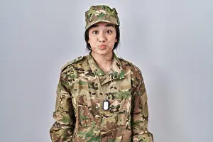 Amusing Prints: Young south asian woman wearing camouflage army uniform puffing cheeks with funny face