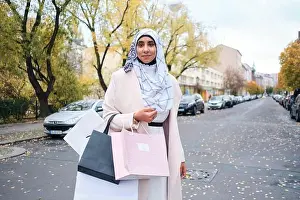 Shopper Prints: Young stylish Arabic woman in hijab confidently looking in camera with shopping bags on street