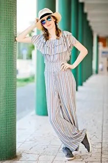 Young teenaged girl in jumpsuit dress posing at colonnade with green pillars, front view