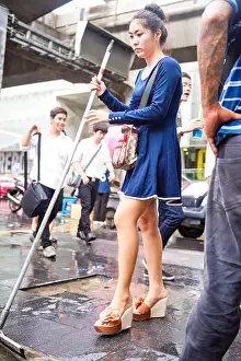 Cleaner Prints: A young Thai girl in a blue dress sweeps the pavement on Sukhumvit Road Bangkok Thailand