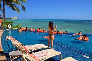 Honeymoon Prints: Young tourists enjoy a summer day relaxing in the infinity pool at a hotel on Waikiki Beach