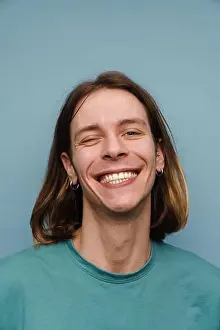 Wink Prints: Young white man wearing t-shirt smiling and winking at camera isolated over blue wall