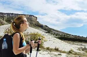 Young Adult Woman Prints: Young woman with backpack and trekking poles in mountains