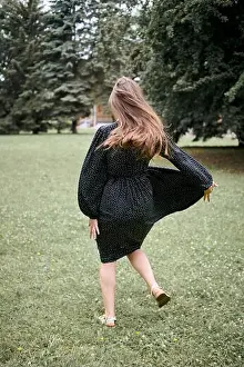 Femininity Prints: Young woman with brown hair twirls on grass in black polka dot dress during daylight
