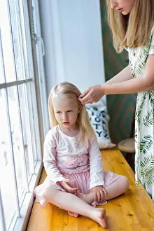 Hairbrush Prints: Young woman brushing pretty girl's hair while sitting in front of window