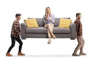 Cushion Prints: Young woman with a cup of coffee sitting on a sofa and two guys carrying the sofa isolated on white background
