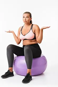 Inspiring Prints: Young woman with excess weight in sporty top and leggings sitting on fitness ball