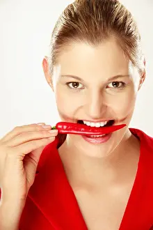 One Young Woman Only Prints: Young woman holding chilies between teeth, close-up, portrait