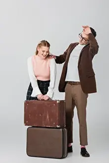 Exhausted Prints: young woman laughing near suitcases and tired boyfriend on grey background