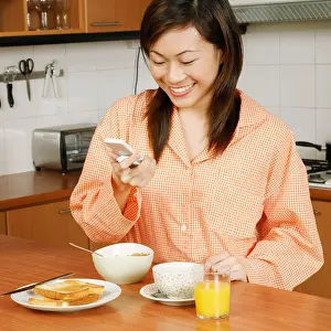Pajamas Prints: Young woman looking at a mobile phone and smiling at a kitchen counter