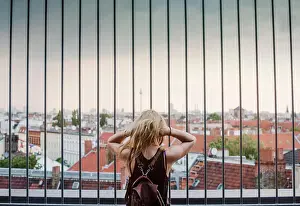 Looking At View Prints: Young woman looking through railings, at view across rooftops, rear view