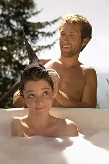 Content Prints: Young woman lying in bathtub, young man washing hair