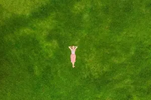 Young woman lying down in the middle of a field and relaxing, drone photo