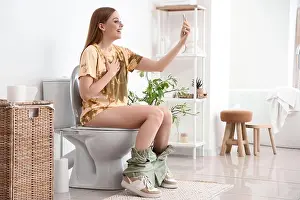 Closet Prints: Young woman with mobile phone sitting on toilet bowl in restroom