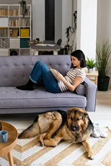 Home Interior Prints: Young woman reading book while dog sitting on carpet at home