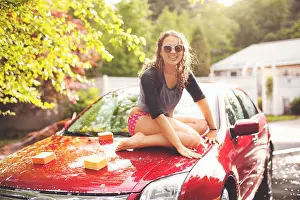 Barefoot Prints: Young woman sitting on car bonnet, portrait