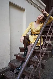 City Background Prints: Young woman sitting on city stairs wearing a yellow dress posing. City street fashion