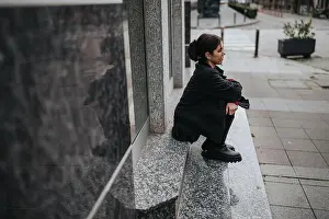 Outdoor Activity Prints: Young woman sitting on a granite ledge in an urban street, contemplative and stylish scene
