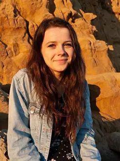 Young woman smiling at golden hour against dramatic coastal rock formations