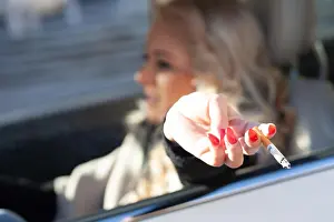 Flicking Prints: Young woman smoking while driving her car flicking ash off her cigarette through the open side window with focus to her
