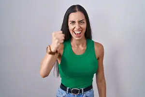Young woman standing over isolated background angry and mad raising fist frustrated