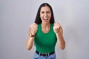Standing Woman Prints: Young woman standing over isolated background angry and mad raising fists frustrated