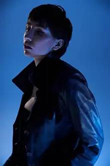 Young woman striking a pose in a black leather jacket against a vibrant blue backdrop