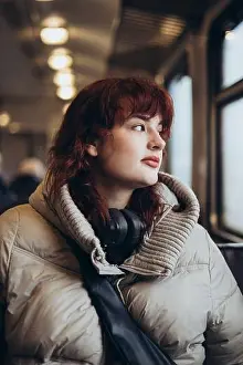 Unrecognizable Prints: A young woman in a warm jacket and headphones sits on a train