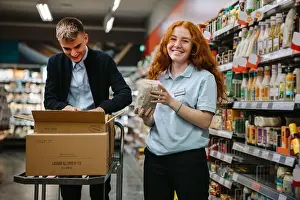 Employees Prints: Young worker restocking the shelves with a colleague in the supermarket